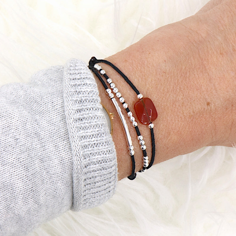 il y a un bracelet femme sur cordon trois tours associé à une pierre de gemmes semi précieuse agate rouge, un jonc et des perles en argent 925 présenté sur un poignet