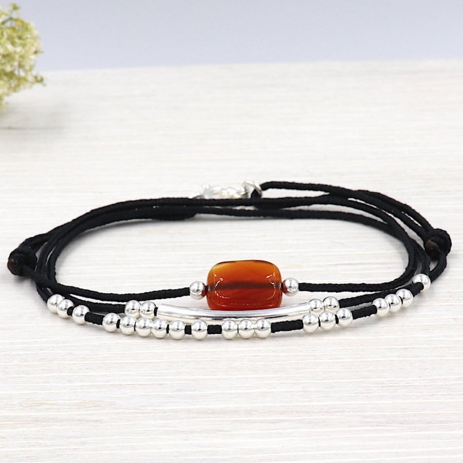 bracelet trois tours réalisé avec un cordon noir haut de gamme associé avec une pierre facettée agate rouge, des perles et un jonc en argent 925 pris en photo sur du bois blanchi