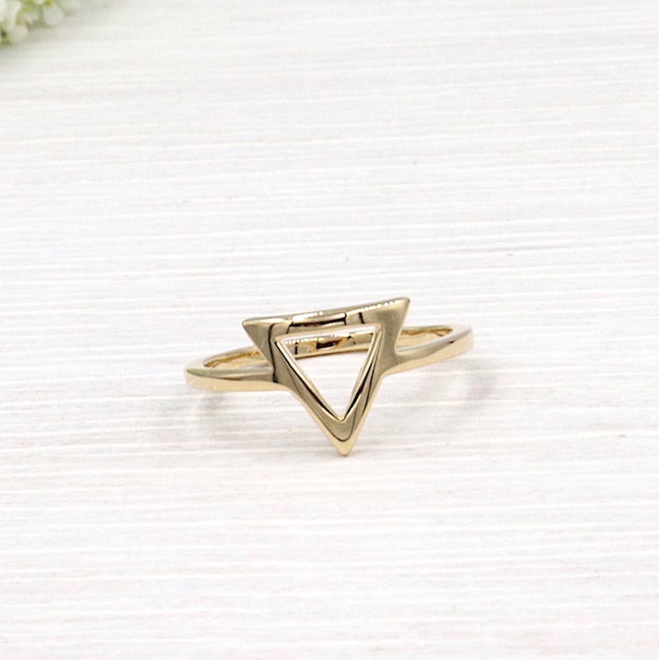il y a une bague forme triangle en plaqué pour femme présentée sur une planche en bois blanchi