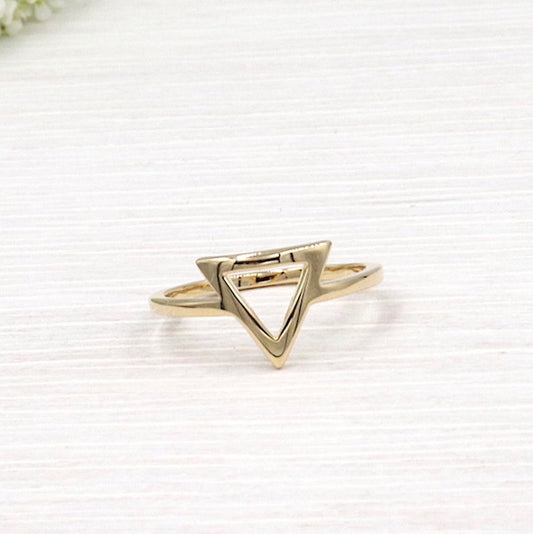 il y a une bague forme triangle en plaqué pour femme présentée sur une planche en bois blanchi