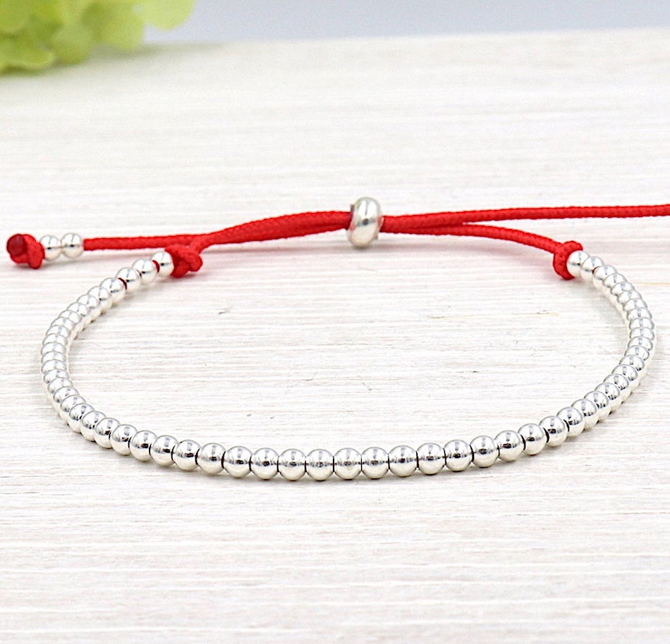 on peut voir un bracelet cordon pour femme réalisé avec des perles en argent 925  se fermant  avec une perle au milieu présenté sur une planche en bois blanchi