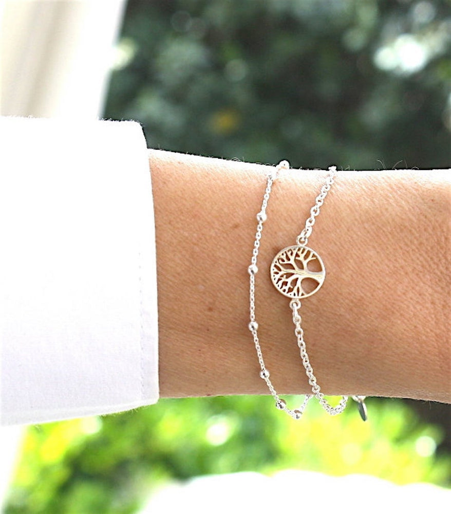 accumulation de bracelets argent 925 sur chaine pour femme un bracelet chaine satellite et un bracelet arbre de vie présenté sur un poignet