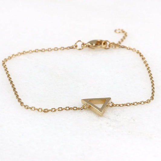 il y a un bracelet femme réalisé avec un triangle  sur chaine en plaqué or présenté sur une plaque de marbre
