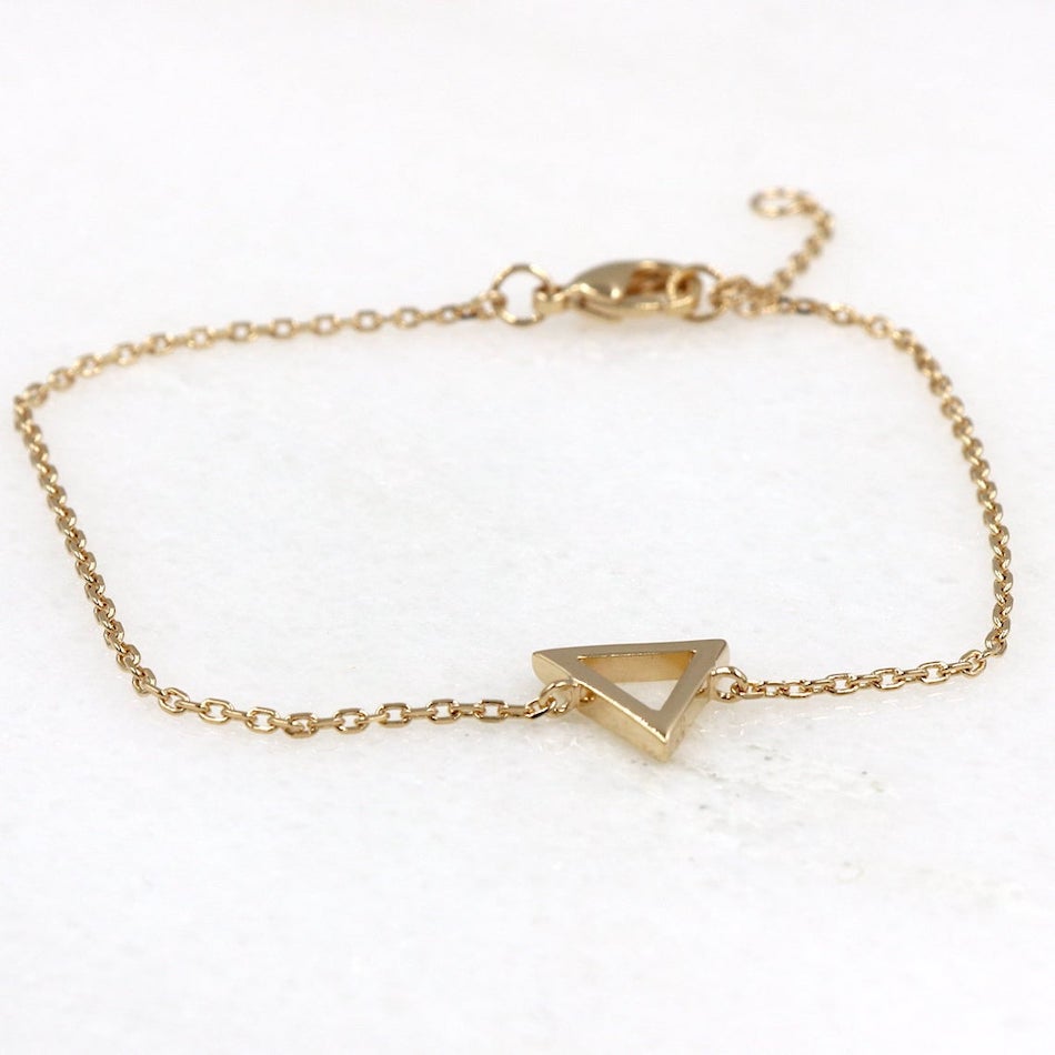 il y a un bracelet femme réalisé avec un triangle  sur chaine en plaqué or présenté sur une plaque de marbre