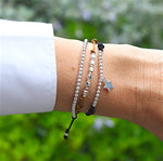 il y a un ensemble de bracelets cordons pour femme avec des perles rondes carrées et une petite étoile en argent 925 sur un poignet avec de la verdure flou en arrière plan