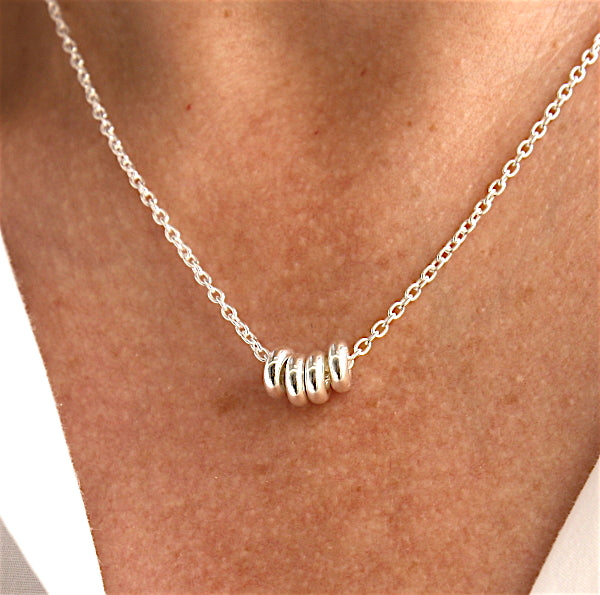 il y a un collier pour femme en argent 925 associé à des donuts sur chaine  présenté dans un décolleté avec une chemise blanche