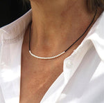 il y a un collier avec des perles en argent 925 sur cordon pour femme  présenté avec une chemise blanche